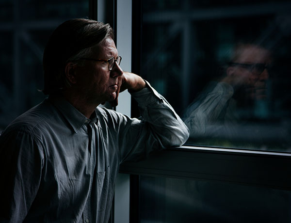 Man resting head on chin looking out a darkened window